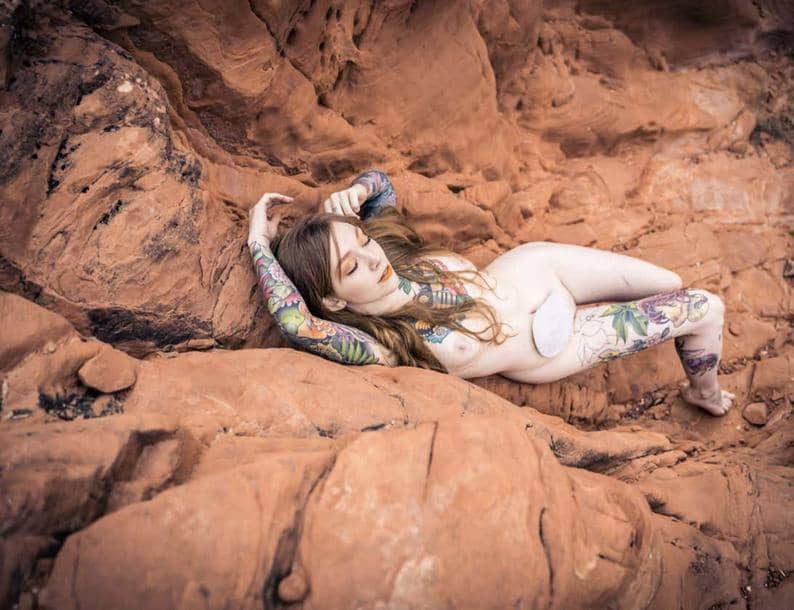 Cam model GoAskAlice appears semi-nude on rocks. 