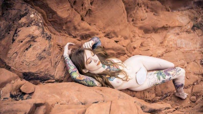 Disabled porn performer and cam model GoAskAlex appears semi-nude on rocks wearing an ostomy bag.