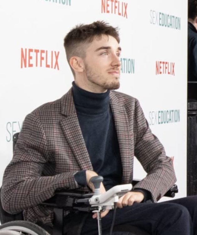George Robinson, who plays Isaac in Sex Education, dressed in a blazer sits in his wheelchair at a Sex Education Netflix premier event.